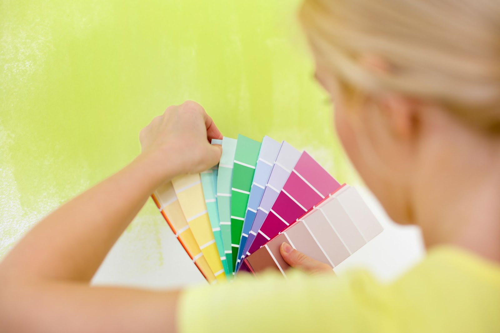 woman compares paint swatches to a paint sample on the wall