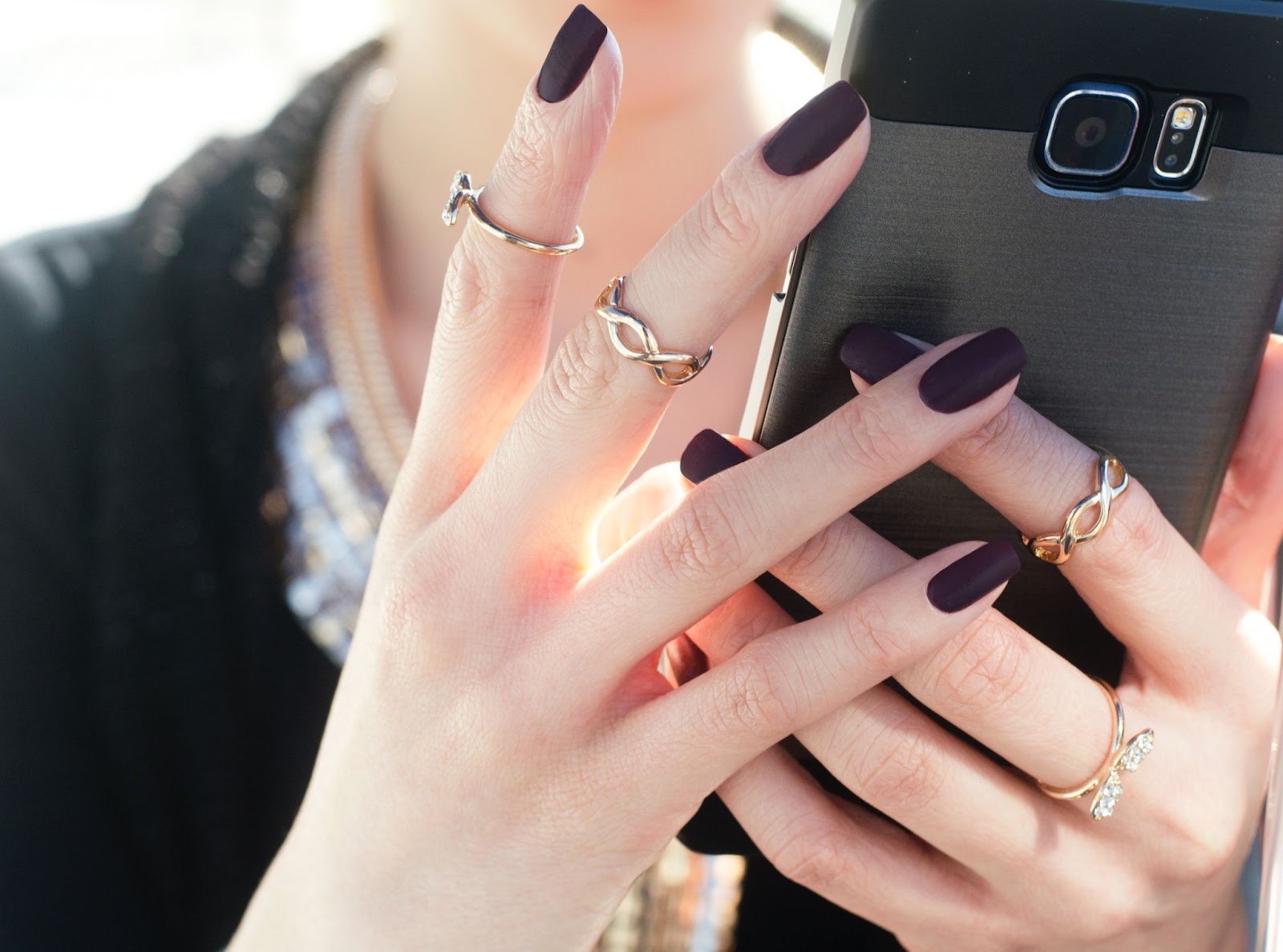 Hands with matte black holiday nails hold smart phone