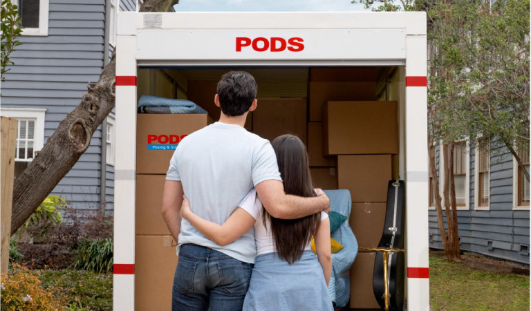 A couple stands together with their arms around each other, facing their loaded PODS moving container.