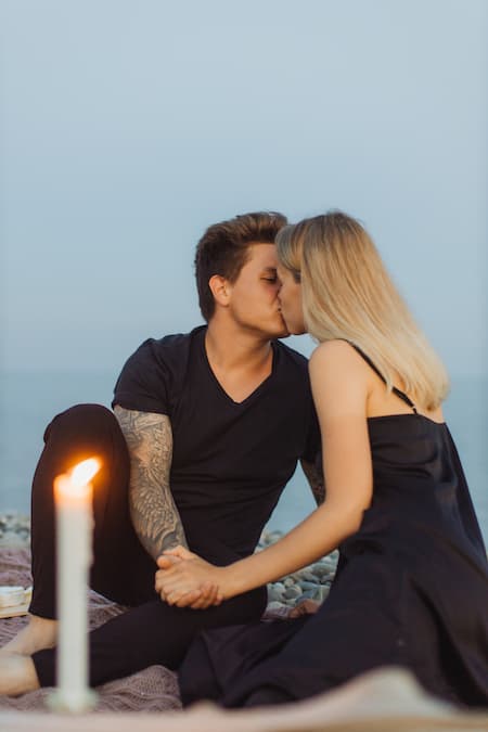 Un homme et une femme qui s'embrassent sur une plage. Une bougie en premier plan qui est floue.