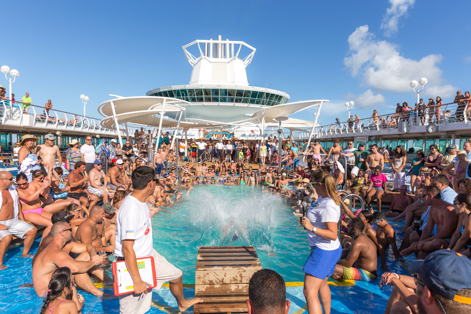 huge crowd of people around an onboard swimming pool of a cruise ship.