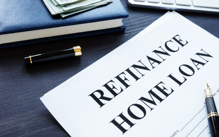 Paperwork for refinancing a home loan on a desk beside a book, a calculator, cash, and an open pen