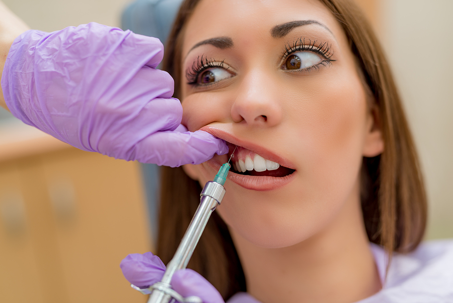 Young woman at dentist looking shocked getting shot of local anesthesia 