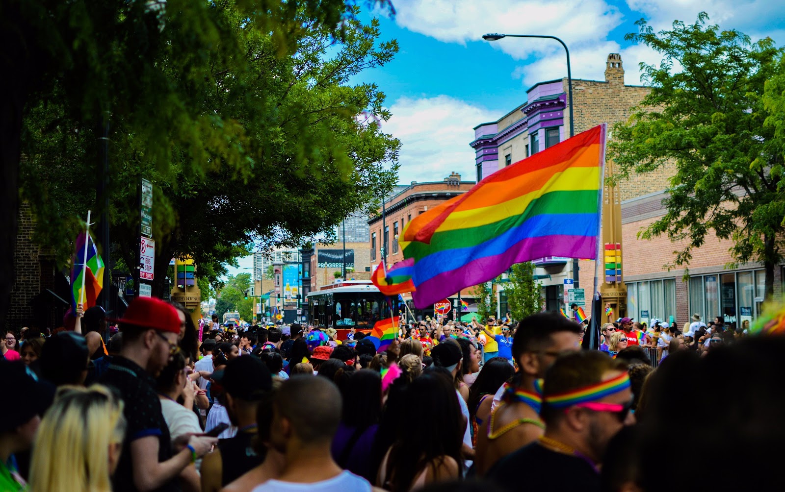 Protesters march in the street while holding rainbow flags.