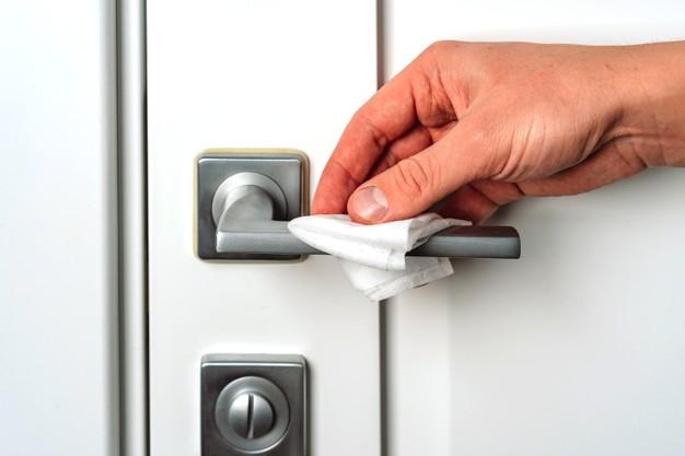 WeServe Hand Wiping The Door Handle With Disinfectant Wipes