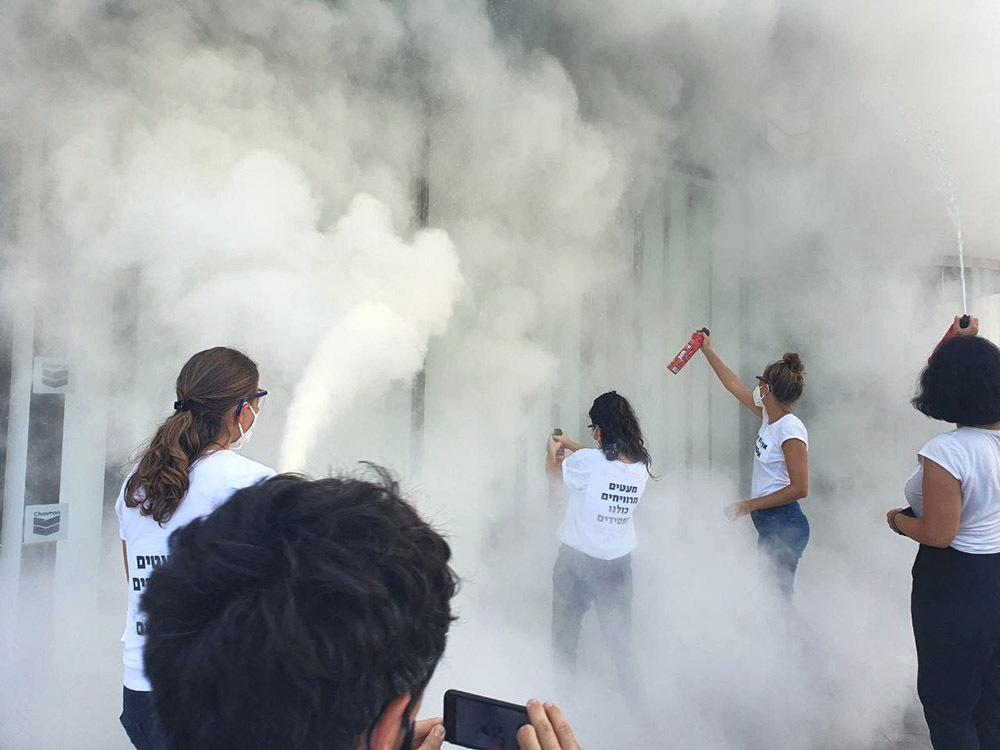 4 women rebels use fire extinguishers to cover a building in white smoke.