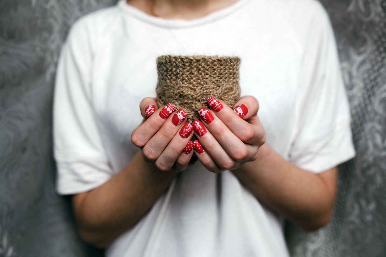 Person hold a candle with yarn knit on the outside and shows off red holiday nail art that features reindeer, sweater prints, and polka dots 