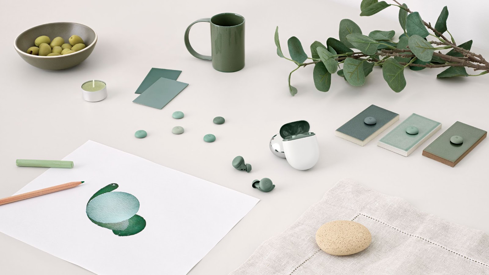 Des pommes vertes dans un bol, une bougie verte, une tasse verte, des aquarelles vertes, des crayons, des feuilles et des bourgeons de pixels verts sont sur une table