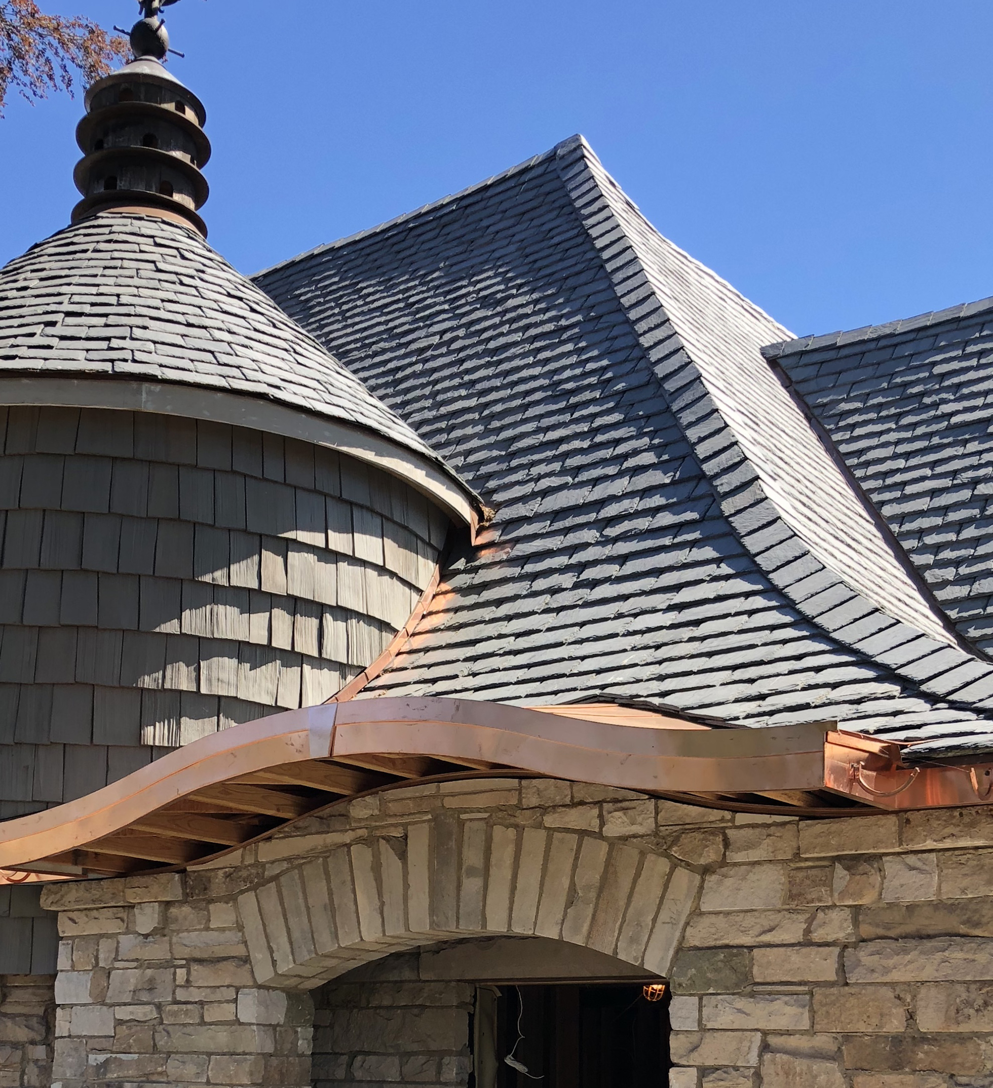 Black roof on stone brick home with copper gutters