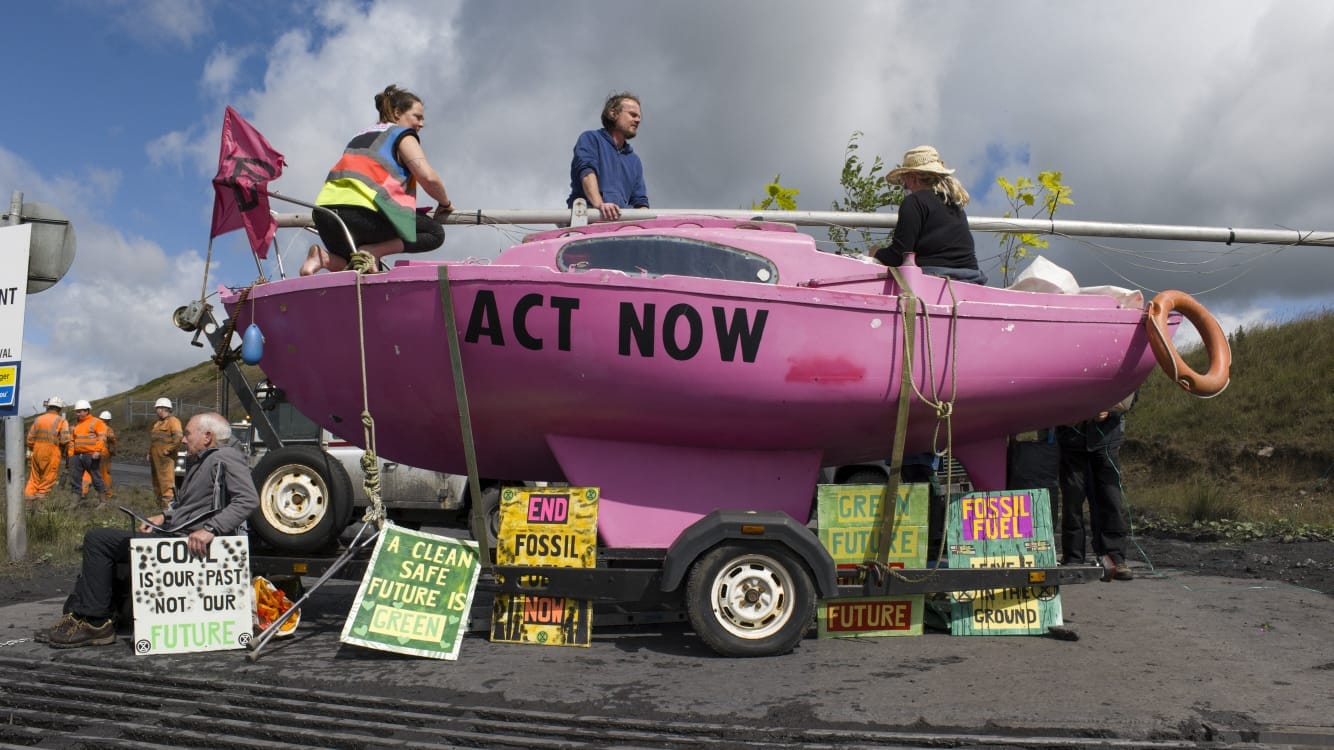 Rebels sit atop and around a pink boat with 'Act Now' on its bow outside a coal mine