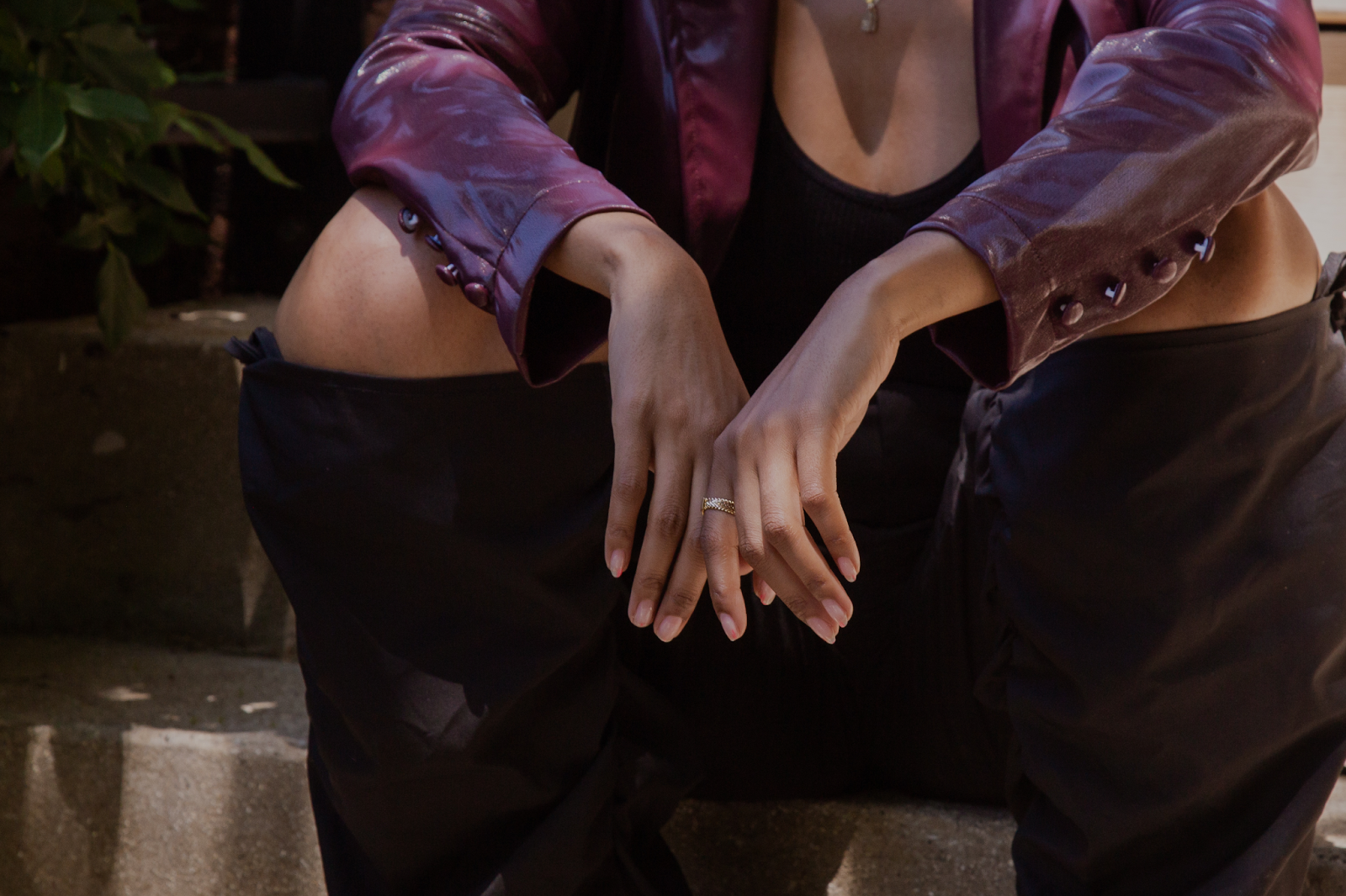 Image: The portrait features Barédu sitting on a shaded, concrete stoop. She is wearing a long burgundy jacket with black pants. Her arms are resting on her knees with both hands meeting in the middle. Image captured and edited by Joshua Johnson.